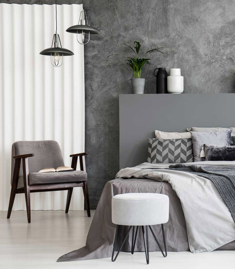Grey armchair and stool near bed with headboard in bedroom inter